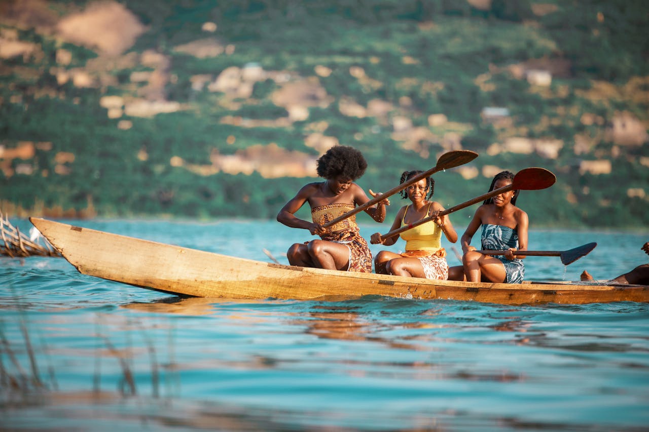 Three women paddle a wooden canoe on a scenic river in Accra, Ghana.