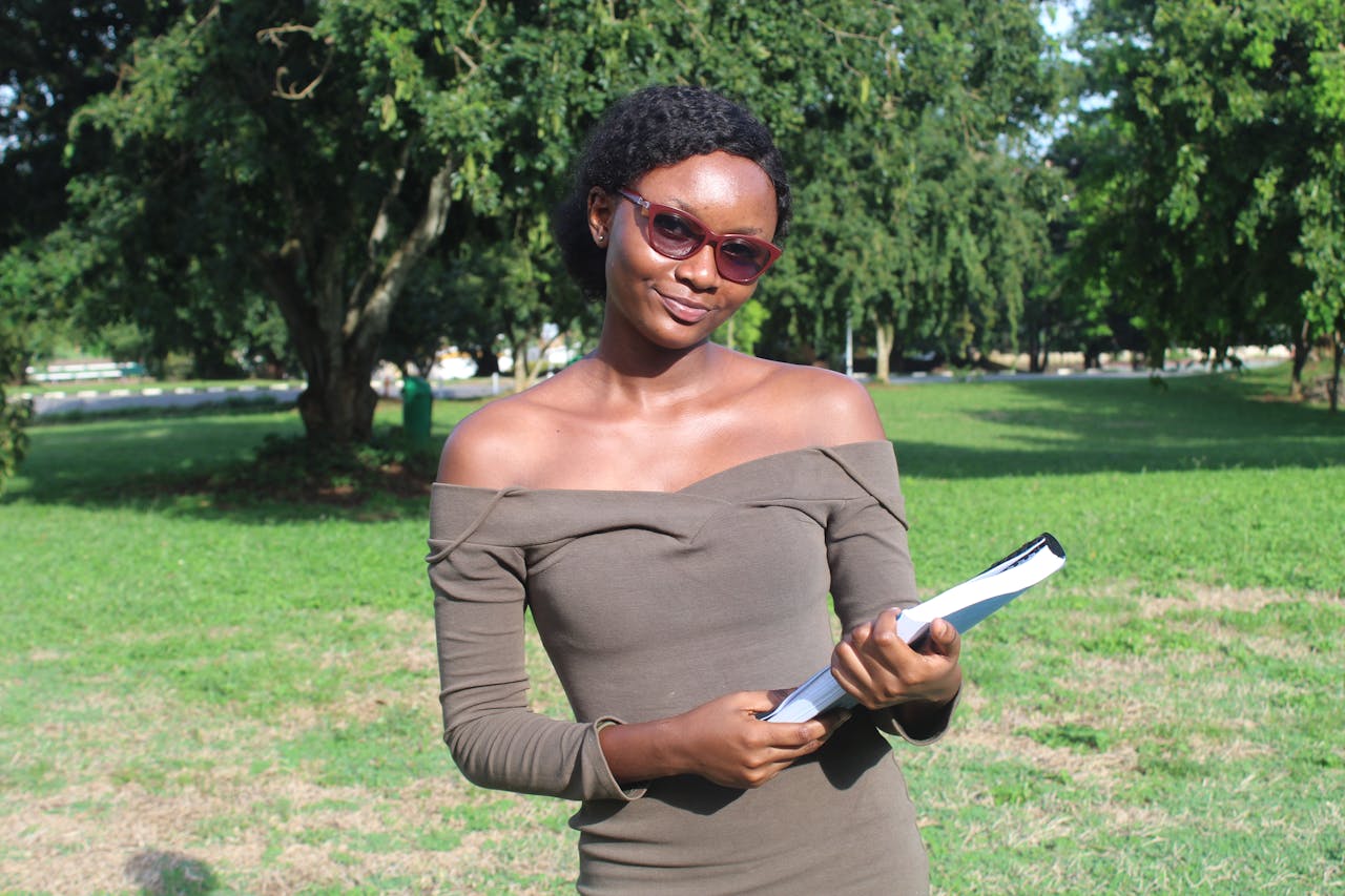 Confident young woman holding books outdoors in Kumasi, Ghana park.
