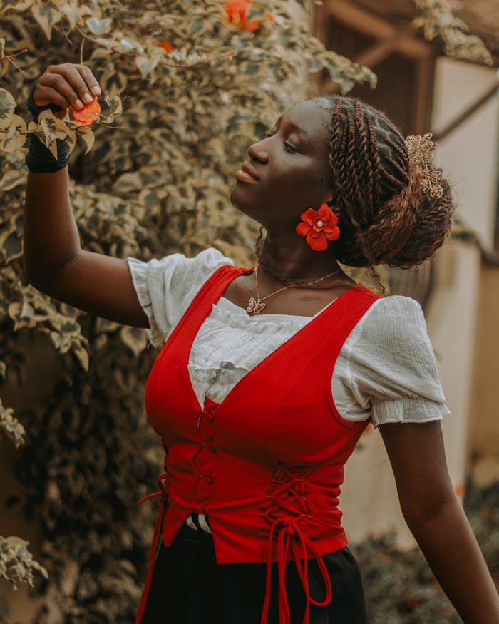 Portrait of a woman in a vibrant red dress, admiring flowers outdoors.